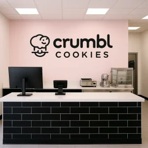 Crumbl Cookies Menu & Prices 2025 – Cost Per Cookie & Packs 12 **Alt text:**
A behind-the-scenes view of Crumbl’s open-kitchen setup, showing bakers preparing fresh cookies on trays, with warm lighting and visible ovens capturing the freshness and transparency of the baking process.